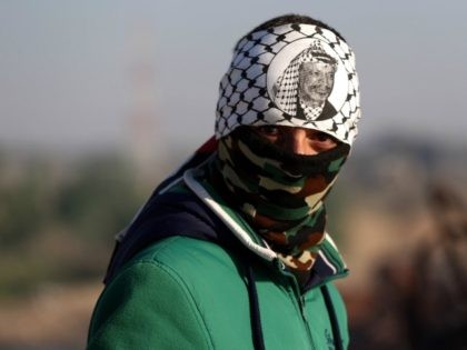 A Palestinian protester, wearing a traditional keffiyeh and bearing the portrait of late P