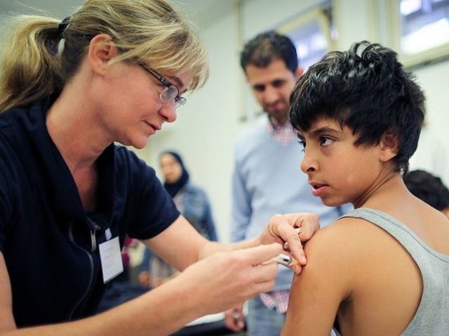 A young Syrian refugee from Damascus gets a vaccination from doctor Susanne Eipper (L) at the State Office of Health and Social Affairs (LAGeSo) in Berlin on October 1, 2015. A record 270,000 to 280,000 refugees arrived in Germany in September, more than the total for 2014. The sudden surge …
