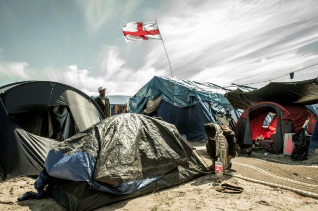Migrants stand next to a flag of England inside the "Jungle" camp for migrants and refugee
