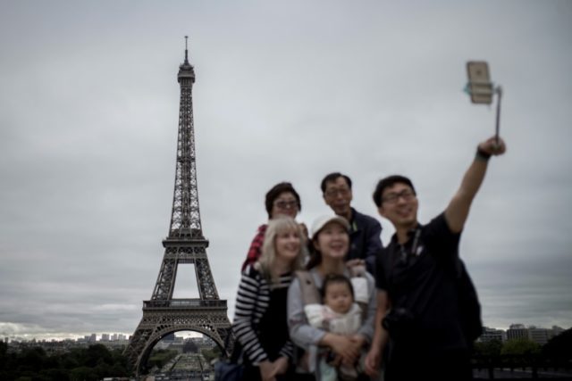 Tourists take selfies in front of the Eiffel Tower in Paris on September 29, 2016