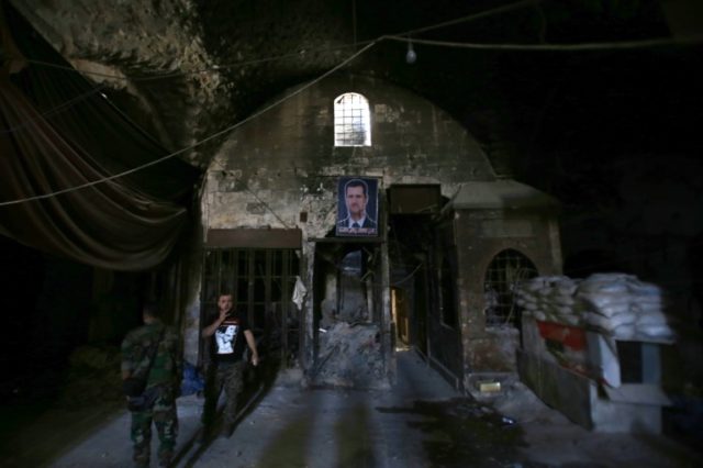 Syrian government soldiers walk under a portrait of Syrian President Bashar al-Assad in th