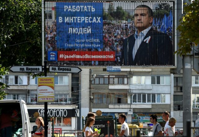 People walk past an election billboard for the United Russia party with a portrait of Crim