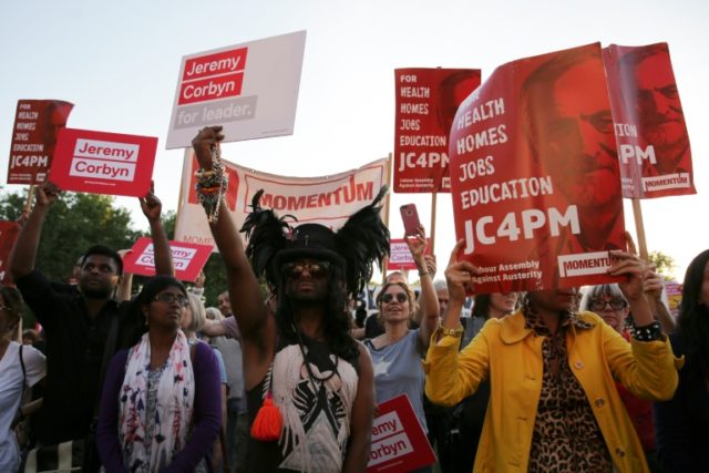Supporters of Jeremy Corbyn hold up placards showing the Momentum logo as they cheer at a