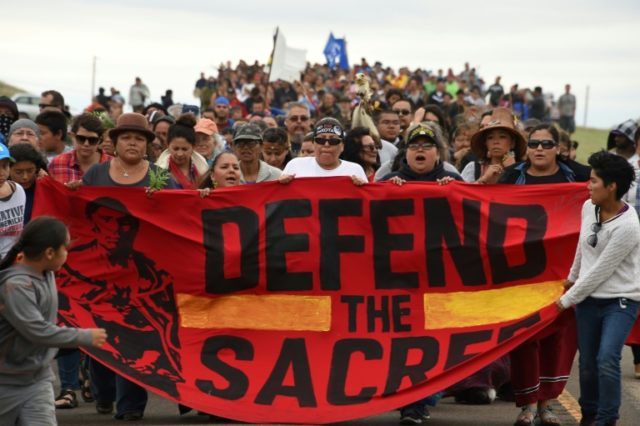 Native Americans marching to a sacred burial ground, disturbed by bulldozers building the