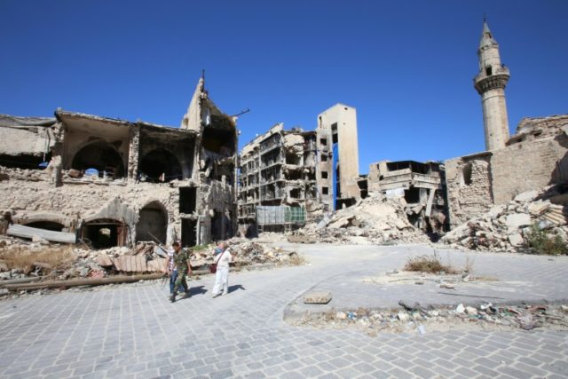 A Syrian government soldier and unidentified people walk in the damaged Khan al-Wazir mark