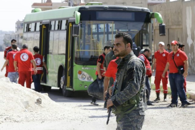 A Syrian soldier stands guard as Red Crescent members wait for opposition fighters and the