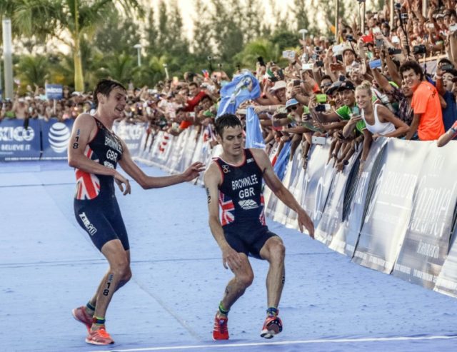 British athlete Alistair Brownlee (L) helps his brother Jonathan (R) as they cross the lin