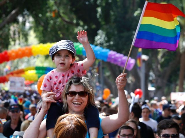 A woman carrying a child on her shoulder waves a rainbow flag during the opening event of the annual Gay Pride parade in the Israeli city of Tel Aviv, on June 3, 2016. - A carefree and cosmopolitan crowd of tens of thousands of homosexuals, transsexuals and supporters took part …