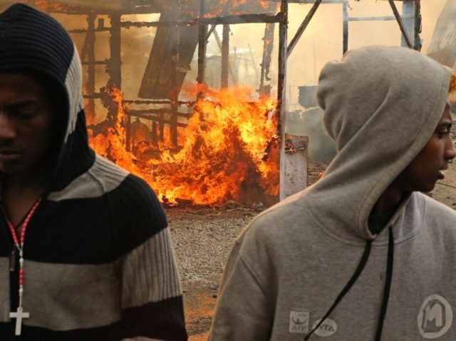 Migrants walk past burning makeshift shelters during fires at the "Jungle" migra