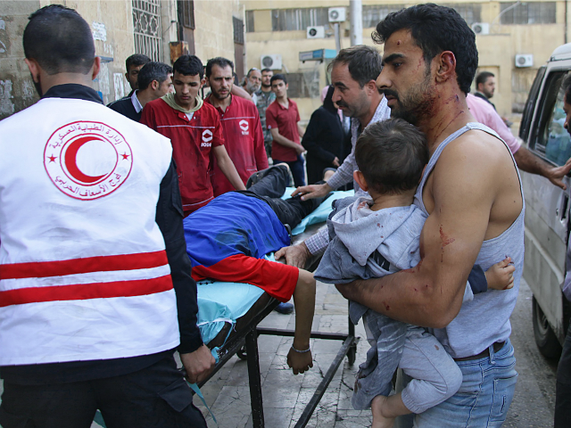 A Syrian man carries a child as they await treatment at a hospital in the regime-held part