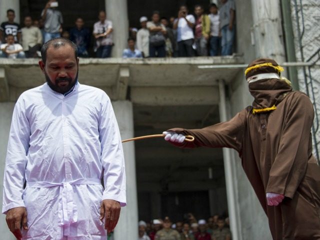 An Indonesian Sharia police whips a man during a public caning ceremony outside a mosque in Banda Aceh, capital of Aceh province on September 18, 2015. Three women and 14 men arrested for sexual offenses and gambling were caned in front of the mosque in full view of the public …