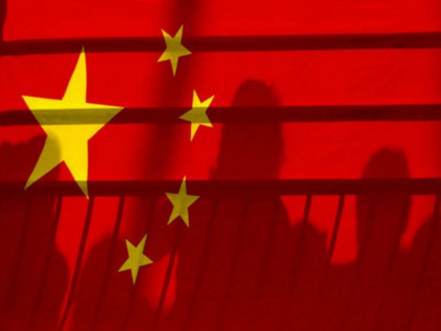 The shadows of spectators are seen through a Chinese national flag during the men's kayak