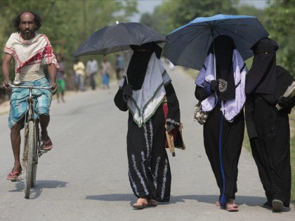 An Indian villager pedals past Burqa clad Muslim students walking to a school at Burhaburh
