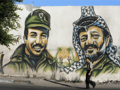 A Palestinian man walks past a graffiti of late Palestinian leader Yasser Arafat (R) and a