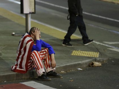 A man dressed in red-white-and-blue sits on the curb during a protest against President-el