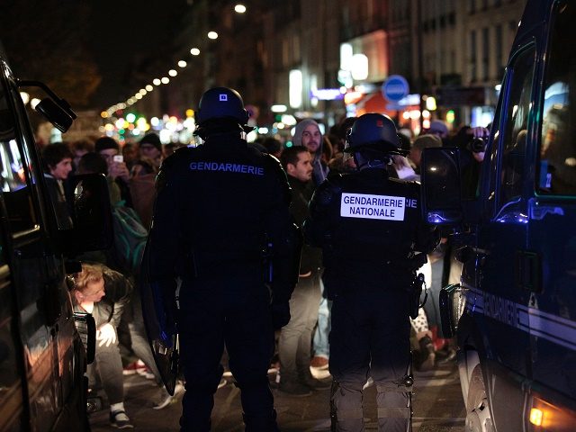 French gendarme stands in front of people during a rally on November 2, 2016 in support of migrants living in a makeshift camp near the Stalingrad metro station in Paris, prior to its evacuation this week. / AFP / GEOFFROY VAN DER HASSELT (Photo credit should read GEOFFROY VAN DER …