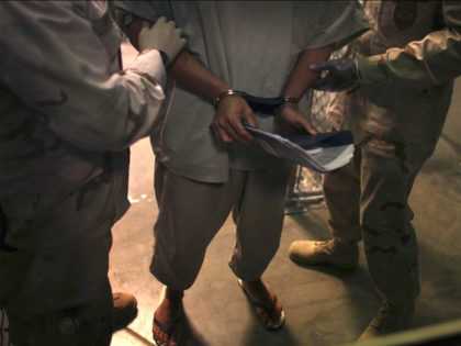 In this March 30, 2010 photo made through one way glass and reviewed by the U.S. military, a handcuffed Guantanamo detainee carries a workbook as he is escorted by guards after attending "Life Skills" class in the Camp 6 high-security detention facility on Guantanamo Bay U.S. Naval Base in Cuba. …
