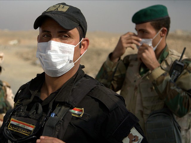 Iraqi troops wear masks as they guard a checkpoint near the village of Awsaja, Iraq, as sm
