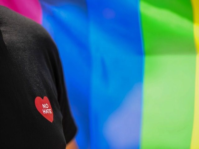 A man displaying 'No Hate' heart on his tee shirt stands near a 'rainbow&#0
