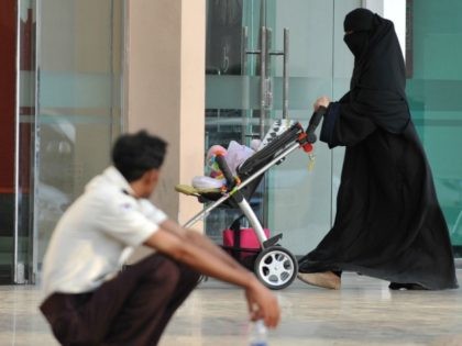 A Saudi woman walks past a foreign worker at the entrance of a shopping mall on November 7