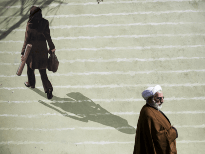 An Iranian cleric walks past a mural depicting a woman in downtown Tehran on February 24,