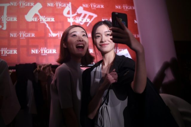 Two models use a mobile phone to take a selfie during China Fashion Week in Beijing on Oct