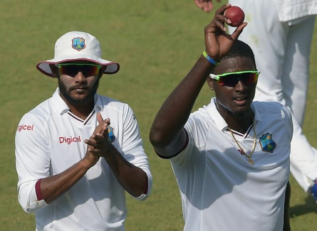 West Indies captain Jason Holder (right) holds the ball aloft after taking five wickets in