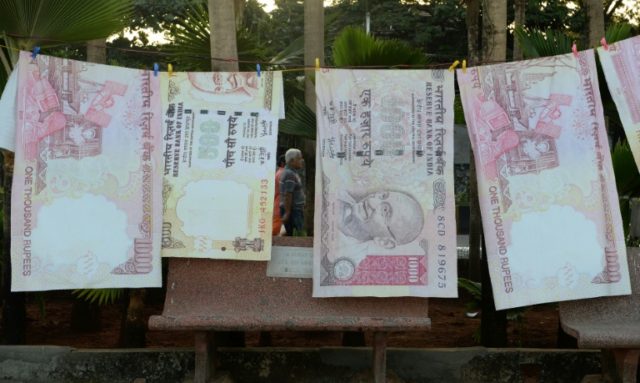 A couple on their morning walk are seen through a gap of replica prints of the demonetised