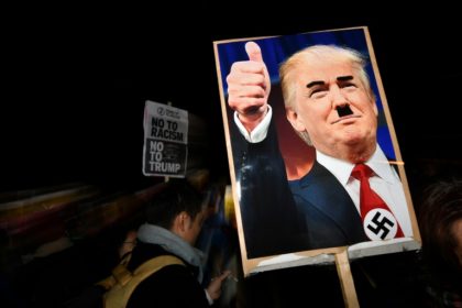 A demonstrator holds a placard showing a picture of US President-elect Donald Trump modified to add a swastika and an Adolf Hitler-style moustache during a protest outside the US Embassy in London