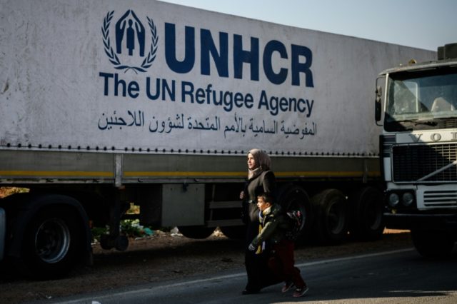 A Syrian woman with her child walks near a Syrian-bound truck loaded with humanitarian aid