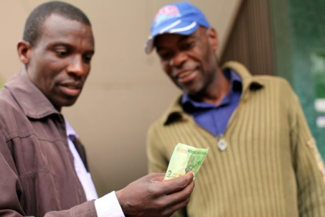 Two men look at a bond note released by the Reserve Bank Of Zimbabwe in the capital Harare