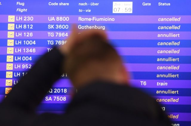A passenger stands in front of a board displaying cancelled flights of German airline Luft