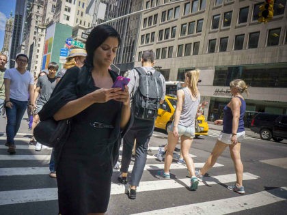 A pedestrian checks her smartphone while crossing a Fifth Avenue intersection in New York