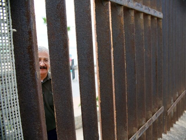 A Mexican National looks through the United States-Mexico Border wall in San Ysidro, California on Saturday, November 19, 2016. / AFP / Sandy Huffaker