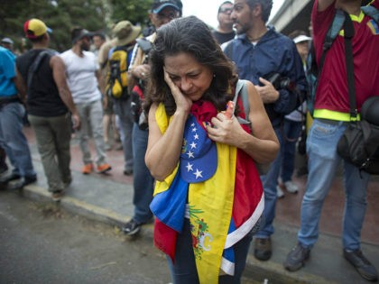 An anti-government protester holds a Venezuelan flag as security forces block the opposition from reaching the National Electoral Council (CNE) in Caracas, Venezuela, Wednesday, May 11, 2016. The opposition is marching to demand election officials start counting signatures that could lead to a presidential recall vote. (AP Photo/Ariana Cubillos)