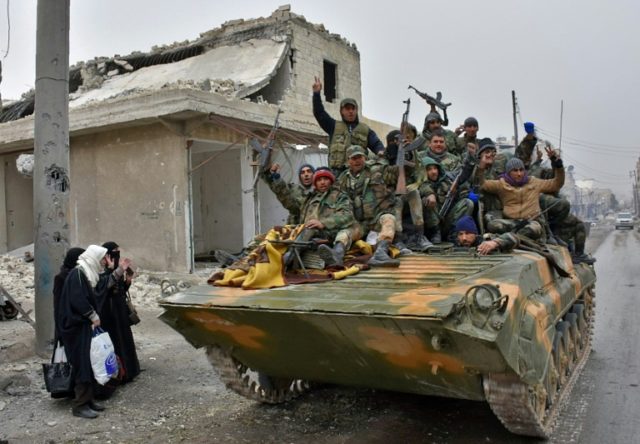 Syrian pro-government forces cheer on a military vehicle driving past residents on Novembe