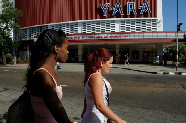 Cubans walk past a movie theater announcing the Havana Latin American Film Festival