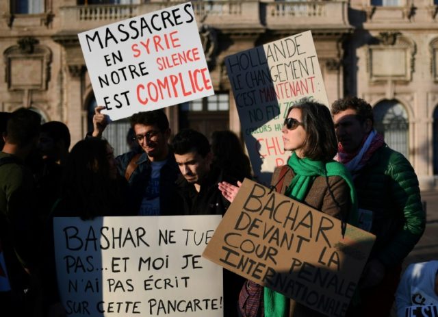People hold signs reading "Massacre in Syria, our silence is an accomplice" and "Bachar to