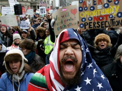 Izzy Berdan, of Boston, center, wears an American flags as he chants slogans with other de