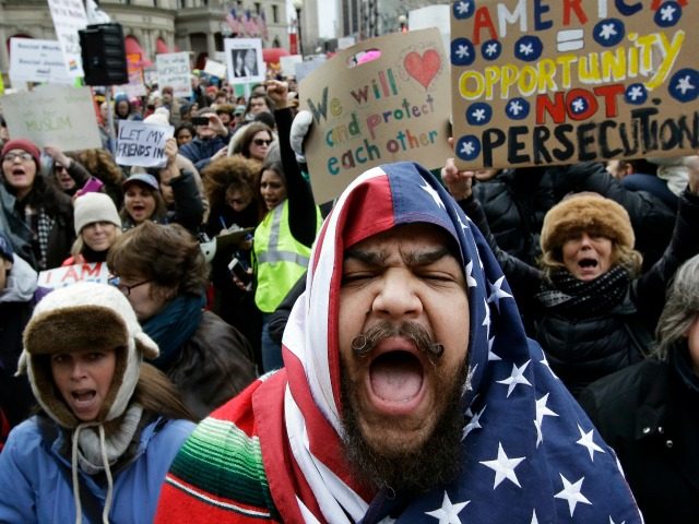 Izzy Berdan, of Boston, center, wears an American flags as he chants slogans with other demonstrators during a rally against President Trump's order that restricts travel to the U.S., Sunday, Jan. 29, 2017, in Boston. Trump signed an executive order Friday, Jan. 27, 2017 that bans legal U.S. residents and …