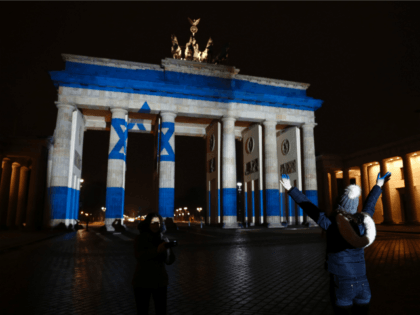 A woman strikes a pose infront of the Brandenburg Gate with the Israeli flag projected onto in Berlin, on January 9, 2017 to pay tribute to the victims of the ramming attack in Jerusalem. Israel was to bury four soldiers on January 9, 2017 killed when a Palestinian rammed a …