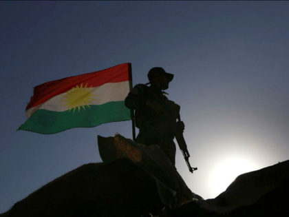 TOPSHOT - An Iraqi Kurdish Peshmerga fighter, next to an Iraqi Kurds flag, holds a positio