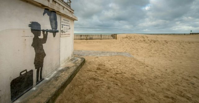 An art piece protected by a plexiglass pane by British artist Banksy, seen on a beach in C