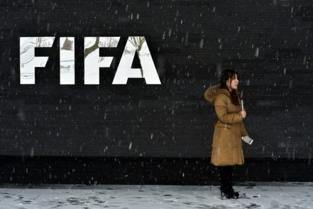 A journalist stands under the snow next to a logo of the International Federation of Assoc