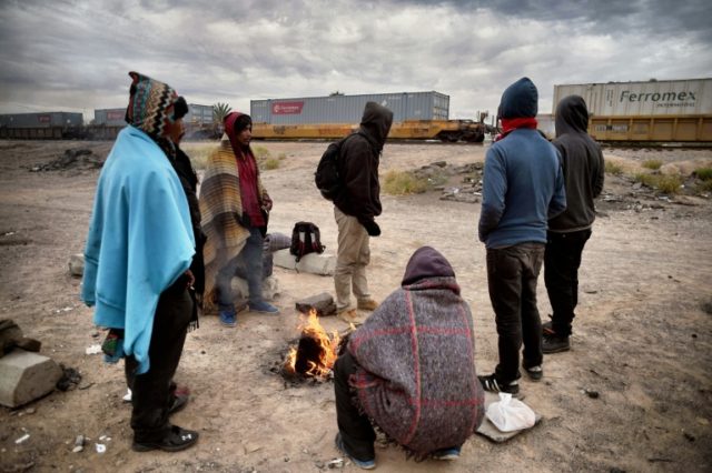 Migrants warm themselves next to a campfire near train tracks in Sonora state, Mexico clos