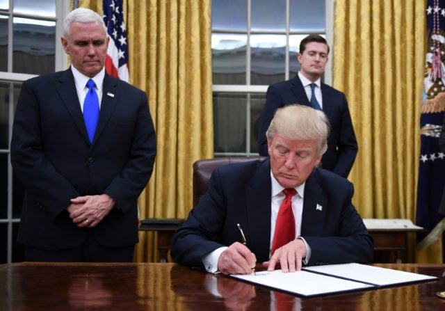 US President Donald Trump signs an executive order as Vice President Mike Pence looks on a
