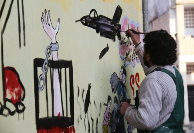 Syrian artist Aziz al-Asmar works on a mural depicting the war ahead of the start of the A