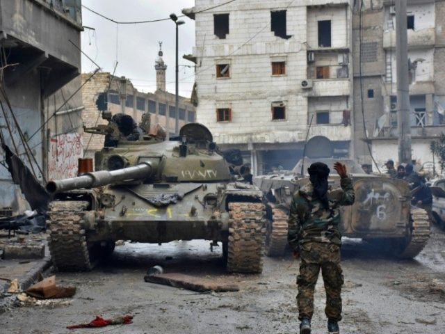 A member of the Syrian pro-government forces gestures to tanks as they patrol the northern