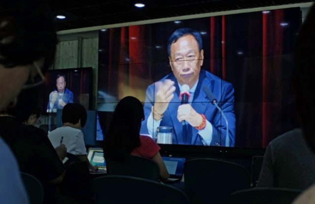 Journalists (in foreground) watch a large video screen showing Terry Gou, founder of Foxco