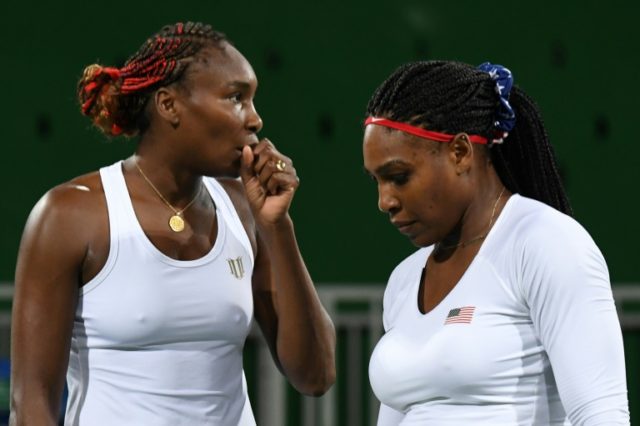 Venus Williams (L) speaks to Serena Williams during their women's first round doubles tenn
